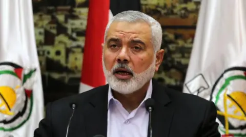 NurPhoto via Getty Images Ismail Haniyeh berbicara melalui mikrofon dengan bendera berkibar di belakangnya