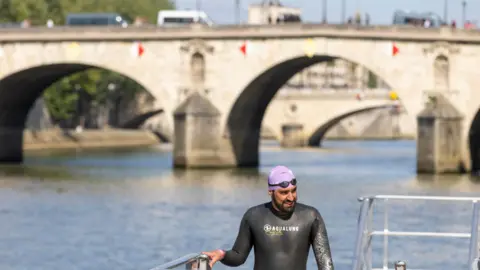 Andre Payne/EPA-EFE/REX/Shutterstock Seorang perenang yang mengenakan pakaian selam dan topi renang warna lavender dengan kacamata di atasnya muncul dari sebuah pemandangan di Paris.