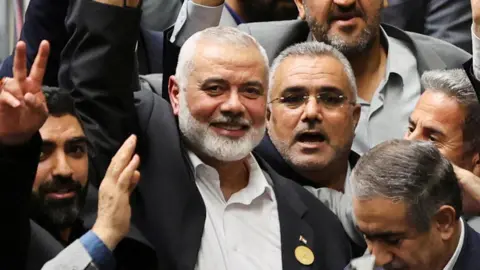 Ismail Haniyeh tersenyum sambil mengangkat tangan di tengah kerumunan orang, melalui kantor berita Asia Barat Reuters