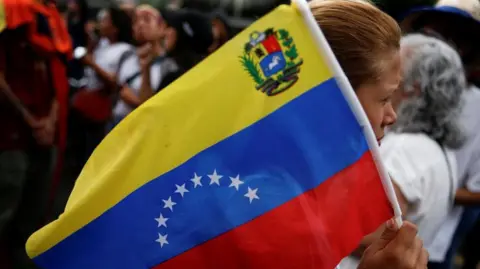 Reuters Seorang demonstran mengibarkan bendera Venezuela saat orang-orang berkumpul untuk memprotes hasil pemilu yang memberi Presiden Venezuela Nicolas Maduro masa jabatan ketiga di Caracas, Venezuela, 30 Juli 2024. 