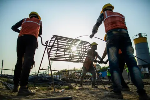 Getty Images Pekerja membangun fondasi di lokasi pembangunan pabrik baru Dixon Technologies Ltd. di Noida, India, Jumat, 22 Maret 2024.  Dixon Technologies Limited, produsen kontrak India, mendapat manfaat dari ledakan baru ini.  Produsen ponsel pintar Tiongkok, Xiaomi Corp.  dan Samsung Electronics Co dari Korea Selatan.  Bisnis dari klien seperti India ingin menggunakan pabriknya untuk memproduksi barang bagi kelas menengah India yang terus berkembang