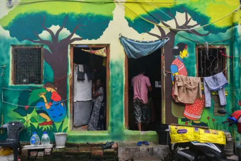 Getty Images Seorang wanita berdiri di dalam rumahnya yang dicat warna-warni di daerah kumuh di Kolkata, India pada 23 Juni 2024. 