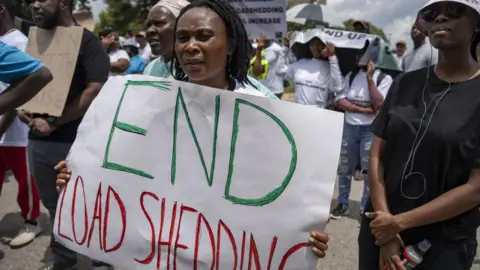 Getty Images Masyarakat memegang spanduk dan memprotes krisis energi setelah pemadaman listrik berkepanjangan di Johannesburg, Afrika Selatan pada 02 Februari 2023.