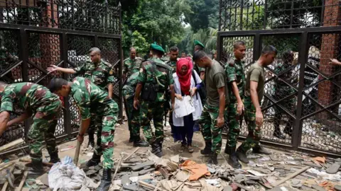 Reuters Anggota tentara membersihkan pintu masuk Ganabhaban, kediaman perdana menteri Bangladesh, sehari setelah Perdana Menteri Sheikh Hasina mengundurkan diri di Dhaka, Bangladesh, 6 Agustus 2024.