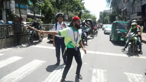 Polisi lalu lintas mahasiswa EPA Bangladesh mencoba mengendalikan lalu lintas setelah mereka tidak muncul untuk menjalankan tugasnya, Dhaka, Bangladesh, 07 Agustus 2024. Berpidato di depan negara, Kepala Staf Angkatan Darat Jenderal Waqar-uz-Zaman mengumumkan pada 05 Agustus.  Perdana Menteri Sheikh Hasina telah mengundurkan diri setelah berminggu-minggu terjadi kerusuhan dan pemerintahan sementara akan dibentuk untuk menjalankan negara.  Sekretaris Pers Presiden Bangladesh mengumumkan pada tanggal 7 Agustus bahwa Muhammad Yunus telah terpilih sebagai pemimpin sementara Bangladesh setelah pengunduran diri mantan Perdana Menteri Bangladesh Sheikh Hasina.  Dhaka, Bangladesh - 07 Agustus 2024 setelah pengunduran diri Perdana Menteri Bangladesh.