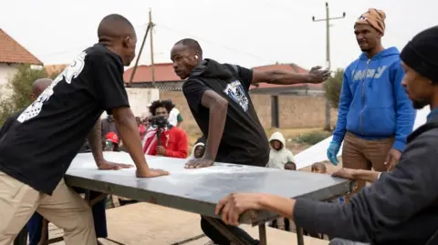 James Oatway / Reuters Seorang peserta bersiap menghadapi pukulan dalam kompetisi adu tamparan di kotapraja Kagiso, sebelah barat Johannesburg, Afrika Selatan, pada 4 Agustus 2024.