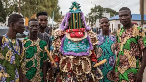     Yannick Foley / AFP Pengunjung berpose dengan kostum Yoruba dan topeng Egungun saat festival di Porto-Novo, Benin - Minggu 4 Agustus Kostum Yoruba dan karakter bertopeng saat festival di Porto-Novo, Benin - Minggu 4 Agustus 2024