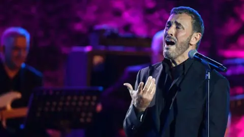     Fethi Belaid / AFP Penyanyi Irak Kadim al-Sahir tampil pada Festival Internasional Kartago di Teater Romawi Kartago di pinggiran ibu kota Tunisia, Tunis, pada 3 Agustus 2024.