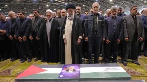 EPA Pemimpin Tertinggi Iran Ayatollah Ali Khamenei dan yang lainnya berdiri di belakang peti mati pemimpin Hamas Ismail Haniyeh yang terbunuh di Teheran (01/08/24).