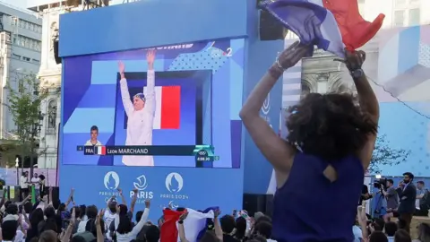 Getty Images Seorang wanita di latar depan bersorak saat perenang Leon Marchand muncul di layar lebar