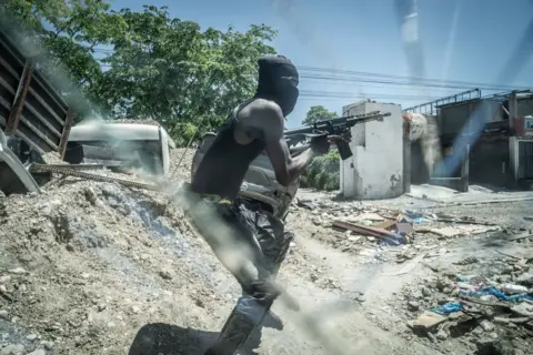 Getty Images Seorang anggota geng G-9 bersenjata berdiri di barikade jalan yang dijaga ketat di kawasan pusat kota Delmas 6 pada 9 Mei di Port-au-Prince.