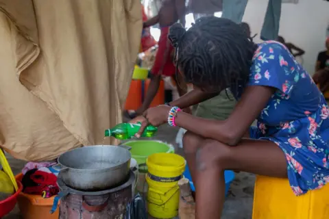 Getty Images Seorang wanita memasak di sebuah kamar di kamp pengungsi di Port-au-Prince.