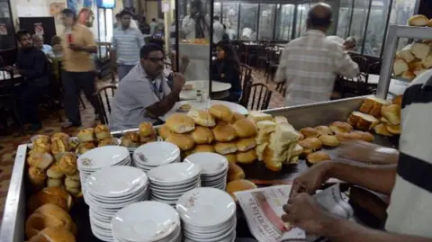 Getty Images B. Merwan & Co. di Mumbai. Pelanggan India menunggu saat seorang karyawan di Kafe Irani mengemas bun maska ​​​​- roti mentega