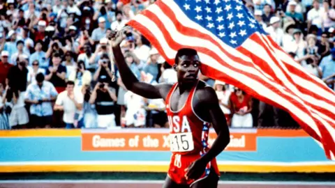 Getty Images Carl Lewis memegang bendera AS di lintasan atletik