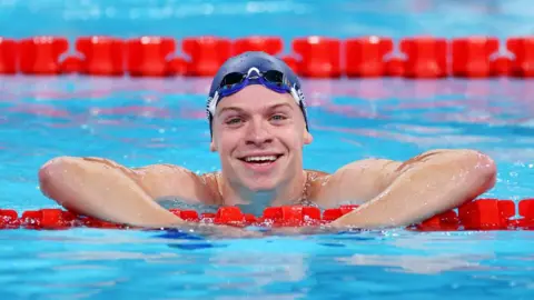 Getty Images Leon Marchand tersenyum ke arah kamera dari kolam