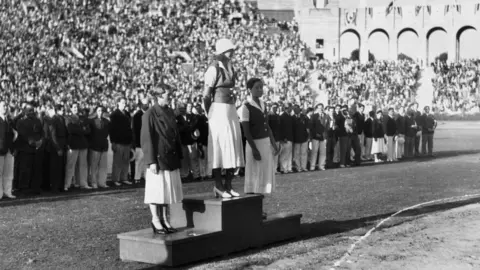 Getty Images Willie den Ouden dari Belanda, peraih medali emas Helen Madison dari AS dan Eleanor Saville dari AS berdiri di podium pemenang Olimpiade 1932 untuk nomor renang gaya bebas 100m