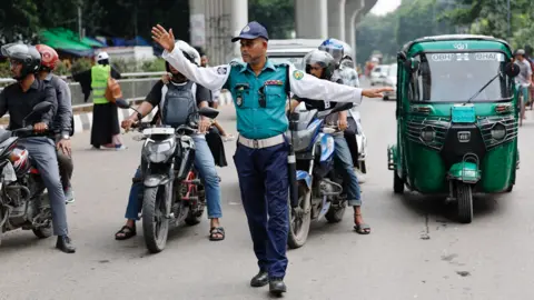 Reuters Seorang petugas polisi lalu lintas melambai ke kendaraan di persimpangan di Dhaka