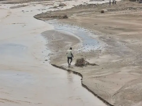     Reuters Seorang pria berjalan di dekat air banjir yang disebabkan oleh hujan lebat di provinsi Hazza, Yaman. 