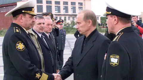 Getty Images Vladimir Putin berjabat tangan dengan Komandan Angkatan Laut Rusia Vladimir Kuroyedov (kiri) setelah tenggelamnya kapal selam Kursk pada tahun 2000