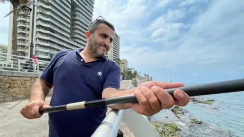 Ayman Sakr memegang pancing di tepi pantai di Beirut, Lebanon.