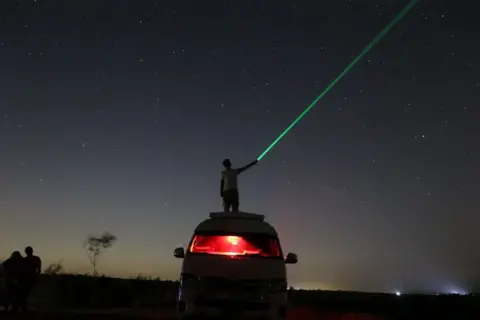 Ahmed Mossad / Getty Images Seorang pria bermain laser sambil melihat galaksi dan bintang di Fayum, Mesir pada 13 Agustus.