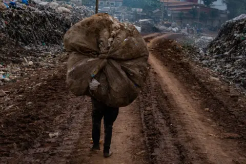 Badru Katumba / AFP Seorang pemulung membawa plastik di kepalanya di lokasi pembuangan sampah di Kampala. 