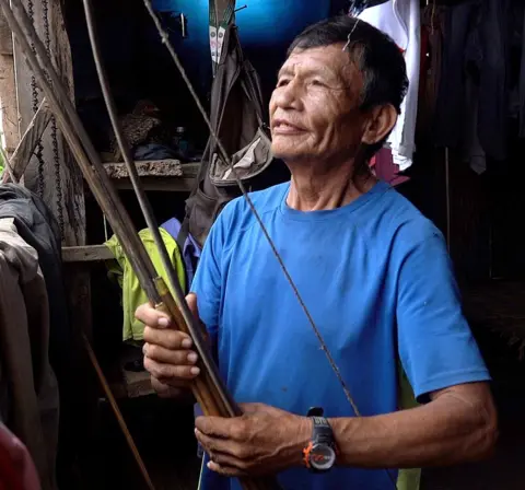 Juan mengenakan kaos biru dan memegang busur 