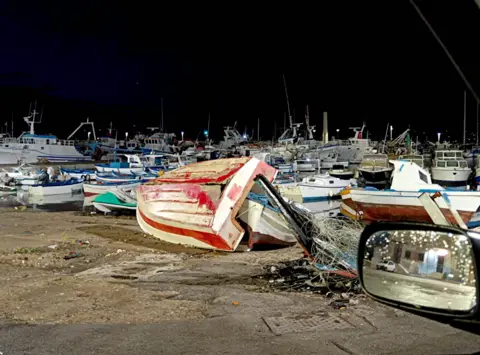 Fabio La Bianca Sebuah perahu kecil terbalik dan kawat pancing membentang melintasi pelabuhan yang penuh dengan perahu.