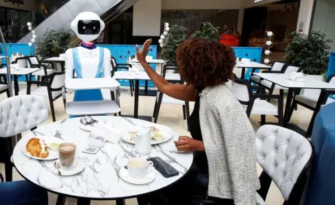 Monica Mwangi / Reuters Caroline Nyaga berterima kasih kepada robot pelayan yang membawakan makanan ke meja makannya. 