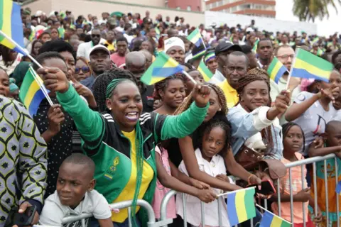 Wilfried MBINAH / AFP Warga mengibarkan bendera saat parade militer untuk Hari Kemerdekaan Gabon.