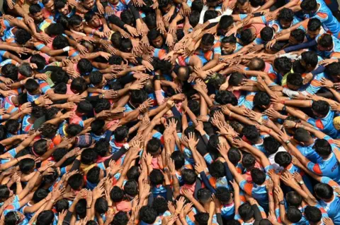 Getty Images Umat Hindu berdoa sebelum membentuk piramida manusia untuk memecahkan dahi-handi (pot yogurt) yang dipegang di udara selama perayaan 'Janmashtami', hari ulang tahun dewa Hindu Krishna, di Mumbai pada 19 Agustus. 2022. (