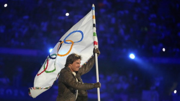 Tom Cruise membawa bendera Olimpiade saat upacara penutupan Olimpiade Musim Panas 2024 di Stade de France pada hari Minggu. (AP)