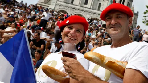 Getty Images Seorang pria dan wanita yang mengenakan baret Prancis memegang anggur merah dan baguette di depan orang banyak