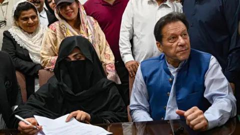 Getty Images Mantan Perdana Menteri Pakistan Imran Khan (kanan) melihat bersama istrinya Bushra Bibi (kiri) saat mereka menandatangani jaminan jaminan dalam berbagai kasus di Kantor Panitera Pengadilan Tinggi di Lahore pada 17 Juli 2023.