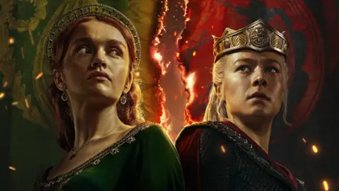 Dua karakter dari House of the Dragon HBO dengan latar belakang api, seorang wanita dengan rambut jahe mengenakan gaun hijau, wanita lain dengan rambut pirang mengenakan gaun chainmail dan mahkota