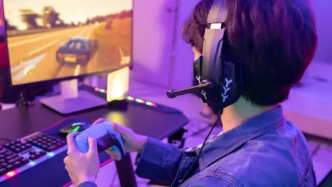 Getty Images Seorang gamer pria memainkan game mengemudi dengan pengontrol game di ruang permainan neon