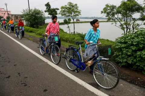 Gadis-gadis desa AP berjalan dengan sepeda yang diterima dari sekolah mereka berdasarkan skema pemerintah di Malancha, distrik 24 Parganas Selatan, India. 