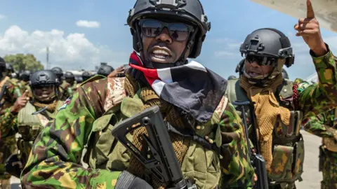 Getty Images Seorang polisi dari tim baru Kenya bereaksi bersama rekannya - Juli 2024