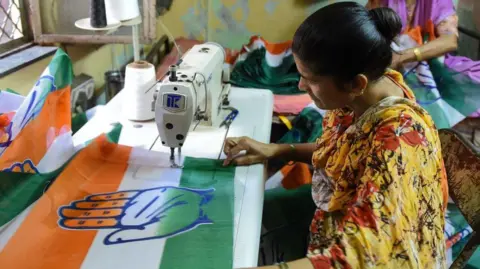 AFP Seorang wanita India menjahit pakaian yang didedikasikan untuk Kongres Nasional India di kediamannya menjelang pemilihan umum India di Ahmedabad, 1 April 2019.