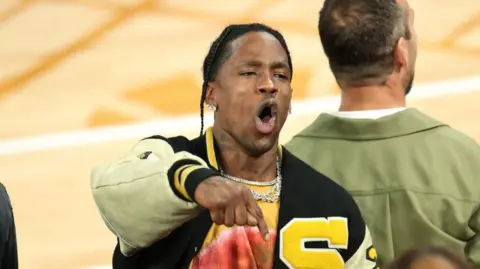 Getty Images Travis Scott mengenakan jaket universitas berwarna hitam dan kuning dengan warna kuning besar 