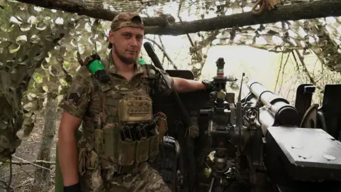 Dmytro, seorang komandan Brigade Garda Nasional ke-15 asal Ukraina, berdiri di samping senjata dengan seragam militer.