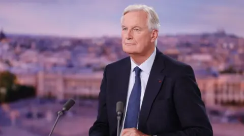 Ludovic Marin/Pool/AFP Michel Barnier menyaksikan sebelum dimulainya siaran berita malam saluran TV Prancis TF1