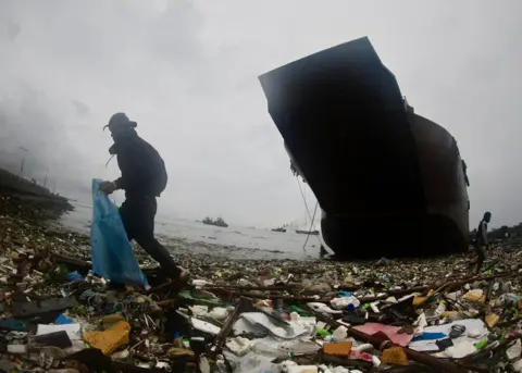 Frans R Malasig / EPA-EFE Seorang penduduk desa mengumpulkan bahan-bahan yang dapat didaur ulang di samping kapal yang tenggelam di Teluk Manila, Filipina