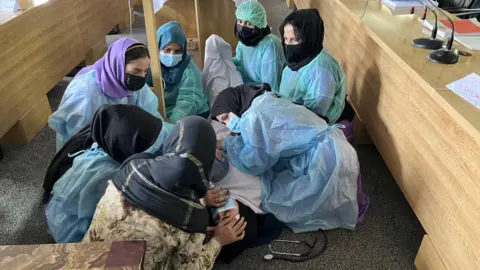 Bidan Afghanistan yang sedang menjalani pelatihan merawat seorang wanita yang tergeletak di tanah