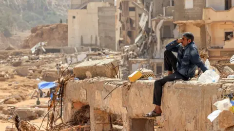 Getty Images Seorang pria duduk di reruntuhan bangunan yang hancur di kota Derna, Libya timur, menyusul banjir mematikan pada 18 September 2023.