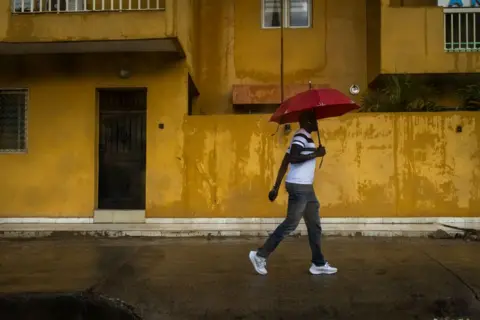 John Wessels / AFP Seorang pria berjalan menyusuri jalan sambil memegang payung saat musim hujan di Senegal.