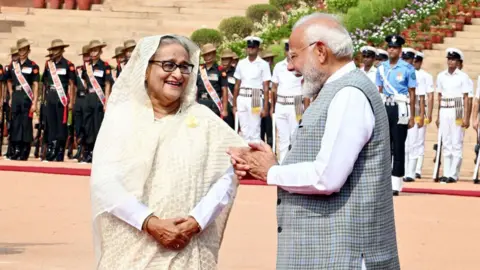 Getty Images NEW DELHI, INDIA - 22 JUNI: Perdana Menteri Narendra Modi berbicara dengan Perdana Menteri Bangladesh Sheikh Hasina dalam resepsi di Rashtrapati Bhavan pada 22 Juni 2024 di New Delhi, India. Perdana Menteri Narendra Modi dan Perdana Menteri Bangladesh Sheikh Hasina membahas hubungan pertahanan, produksi pertahanan, kerja sama dalam memerangi terorisme, manajemen perbatasan dan masalah lainnya dalam pembicaraan bilateral yang diadakan di New Delhi pada hari Sabtu. Perdana Menteri Narendra Modi mengatakan kedua negara fokus pada konektivitas, perdagangan dan kerja sama. Dia mengatakan kedua negara akan fokus pada konektivitas digital dan energi untuk meningkatkan perekonomian mereka. (Foto oleh Arvind Yadav/Hindustan Times melalui Getty Images)