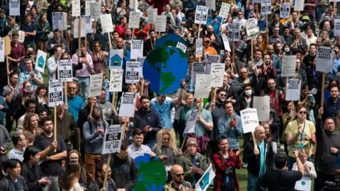 Getty Images Pekerja Amazon berkumpul untuk rapat umum saat pemogokan di kantor pusat perusahaan di Seattle, Washington pada 31 Mei 2023. Seiring dengan PHK dan isu perubahan iklim yang terjadi baru-baru ini, aksi protes telah diorganisir untuk menarik perhatian terhadap kebutuhan kembali ke tempat kerja. 