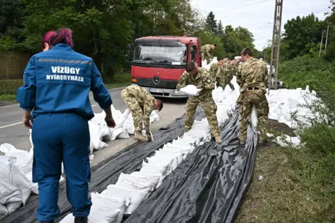 Getty Images Lebih dari selusin tentara berseragam menumpuk karung pasir dan lembaran plastik sebagai penghalang banjir darurat. 