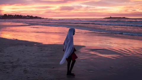 John Wessels/AFP Seorang remaja putri berjalan di pantai di Dakar, Senegal saat perayaan Maulid Nabi Muhammad - Minggu 15 September 2024. 